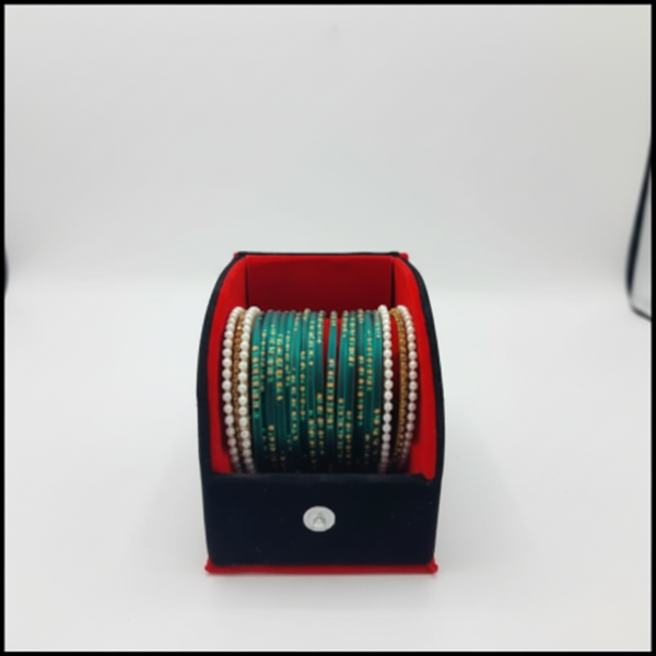 A set of Indian bangles (buckles) displayed in an open black jewelry box with a red interior. The bangles feature green, white, and gold metallic designs.